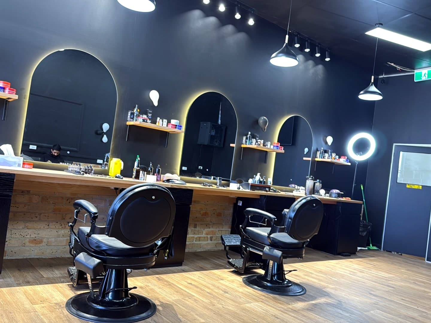 Inside the shop: arched mirrors with warm backlighting, black walls, exposed brick and vintage barber chairs